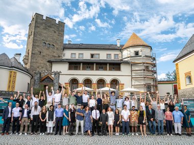 Group picture in front of the picturesque castle. Some participants are raising their hands.