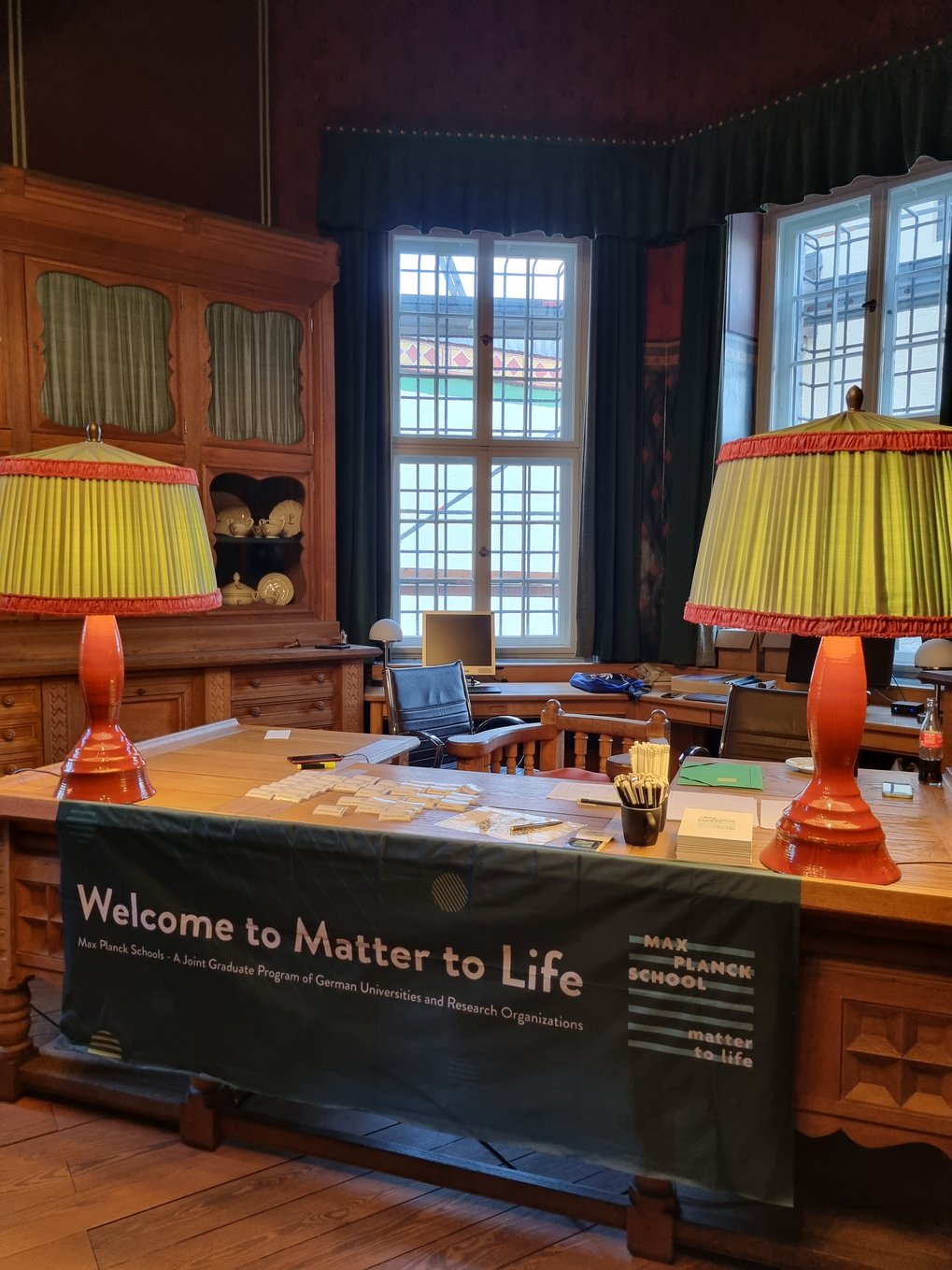 A wooden welcome desk in a historic room of the castle with large windows and ornate furniture. A banner on the desk reads “Welcome to Matter to Life” The desk holds name tags, pens, and informational materials.