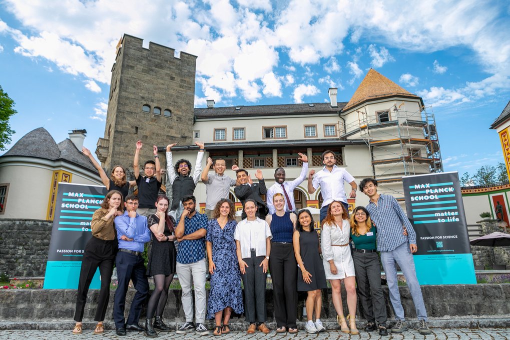 Group picture of the graduates, also using the castle as a backdrop. A few students in the front are hitting the thinking pose, a few in the back are raising their hands.