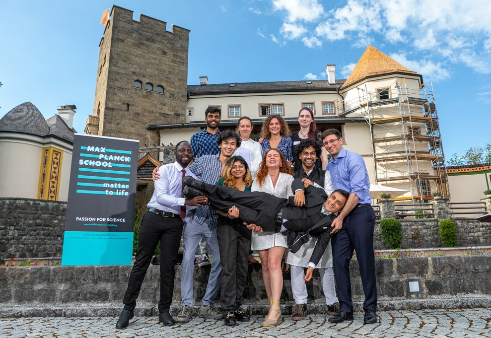 Group picture of ten graduates laughing and holding another fellow student up horizontally in the air.
