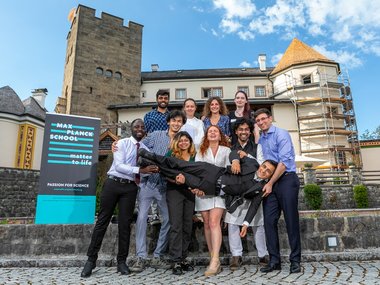 Group picture of ten graduates laughing and holding another fellow student up horizontally in the air.