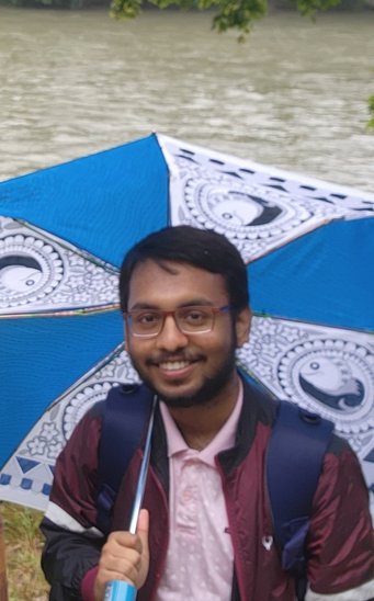 A person carries a vibrant blue and white umbrella with detailed designs, standing in front of a river.