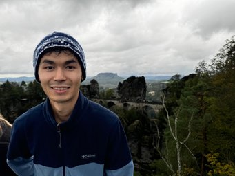 Mussa Yedigenov PhD candidate Mussa, with a stone bridge spans rocky cliffs with a cloudy sky in the background