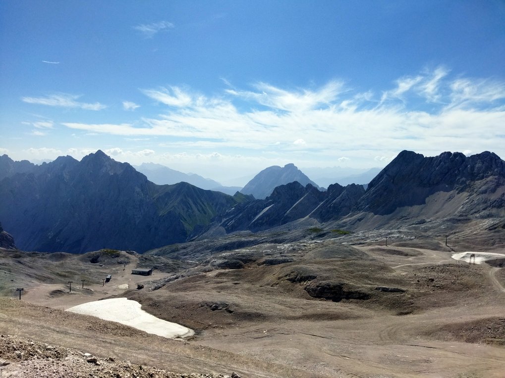 Rocky mountain landscape with clear blue skies, scattered snow patches, and distant peaks.