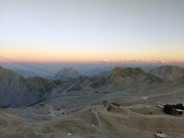 Sunset over rocky mountain landscape with cable car station in the foreground.