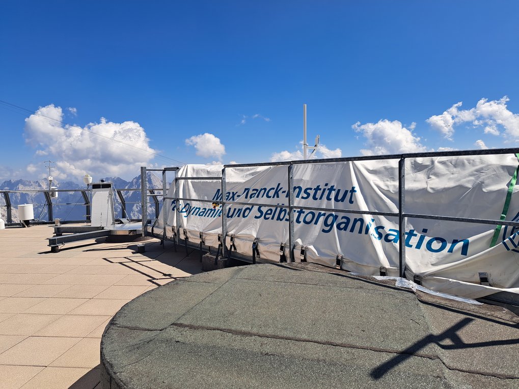 A research facility's rooftop, featuring scientific instruments and a tarpaulin labeled "Max Planck Institute for Dynamics and Self-Organization."