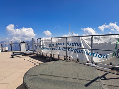 A research facility's rooftop, featuring scientific instruments and a tarpaulin labeled "Max Planck Institute for Dynamics and Self-Organization."