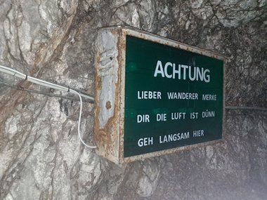 Metal warning sign on a rock face advising hikers: “Dear hiker, please note that the air is thin here, so proceed slowly.”