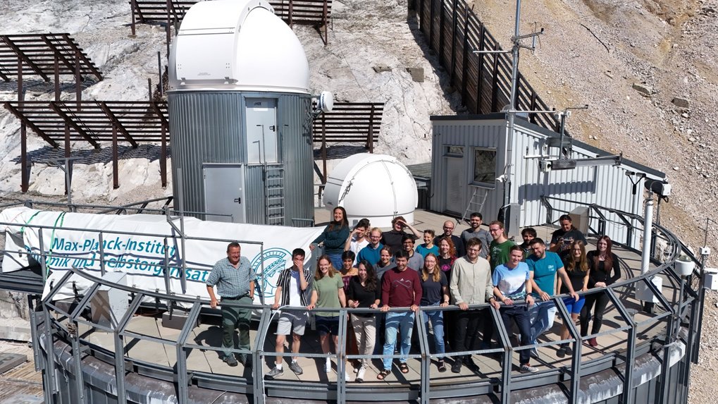 Zugspitze Symposium attendees assembled on a terrace, with observatory domes and a rocky mountain slope in the background.