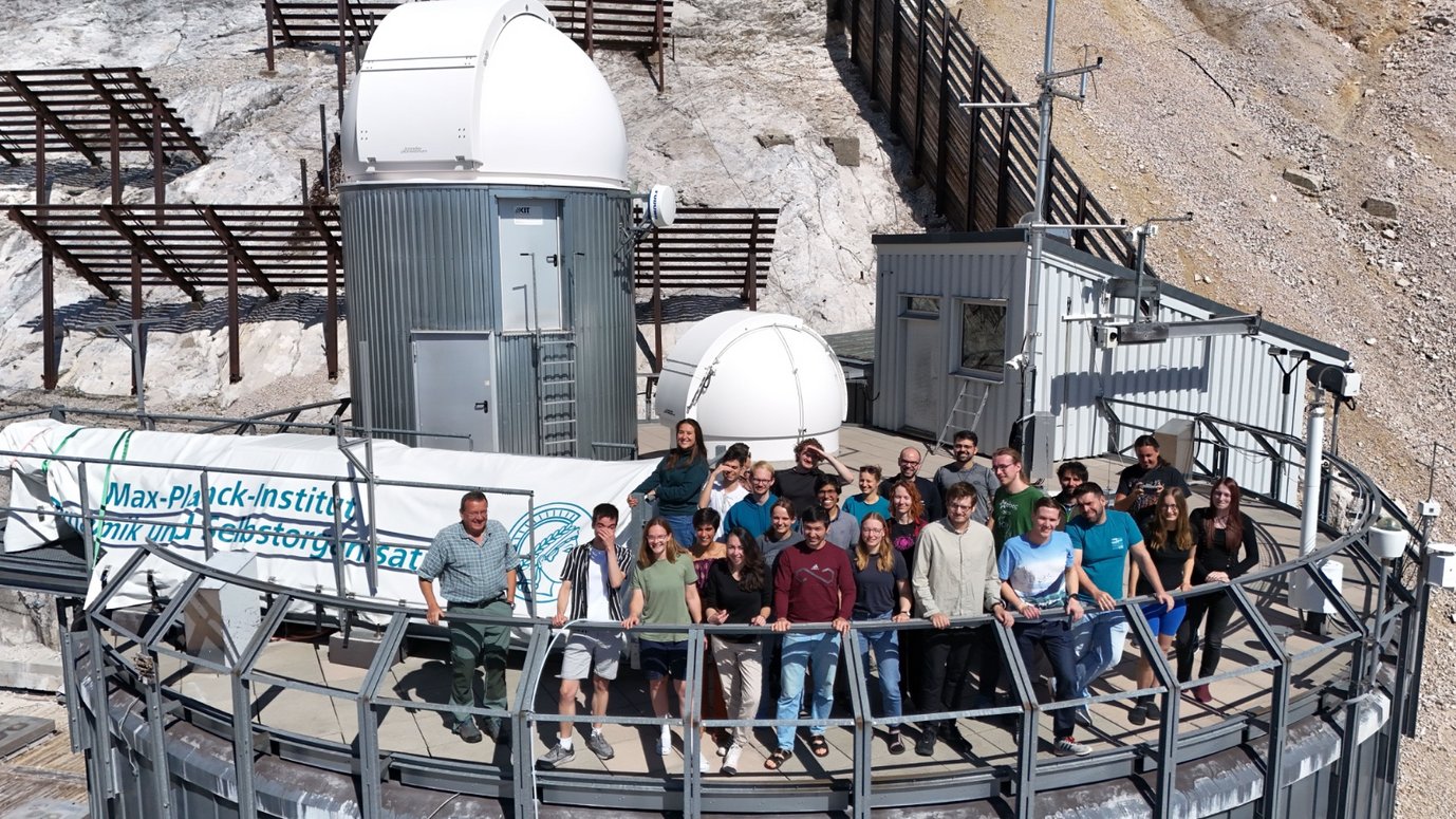 Zugspitze Symposium attendees assembled on a terrace, with observatory domes and a rocky mountain slope in the background.