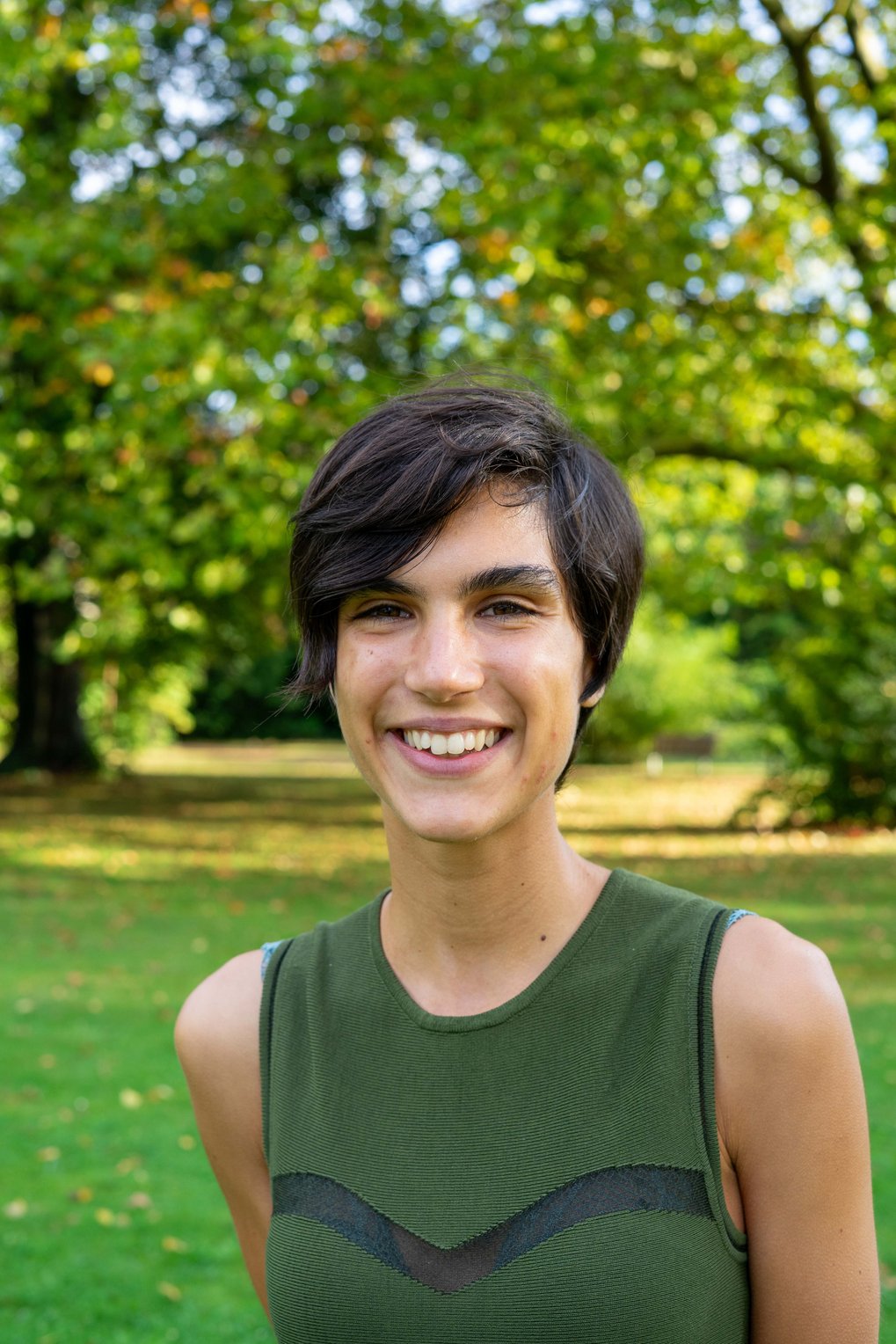 Porträt von Matter to Life PhD Kandidatin Irene Pellini, im Hintergrund eine von der Sonne beschienene Wiese und Bäume 