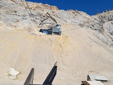 View of a cable car ascending a rocky mountain slope toward the Schneefernerhaus research station on the Zugspitze under a clear blue sky.