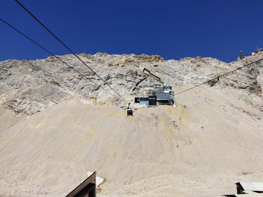 View of a cable car ascending a rocky mountain slope toward the Schneefernerhaus research station on the Zugspitze under a clear blue sky.