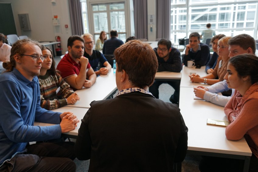 Career round tables in full swing—PhD candidates, Fellows, and plenty of lively conversations. A gathering of individuals seated at tables, engaging in discussions. The room is well-lit by large windows, creating an open atmosphere.
