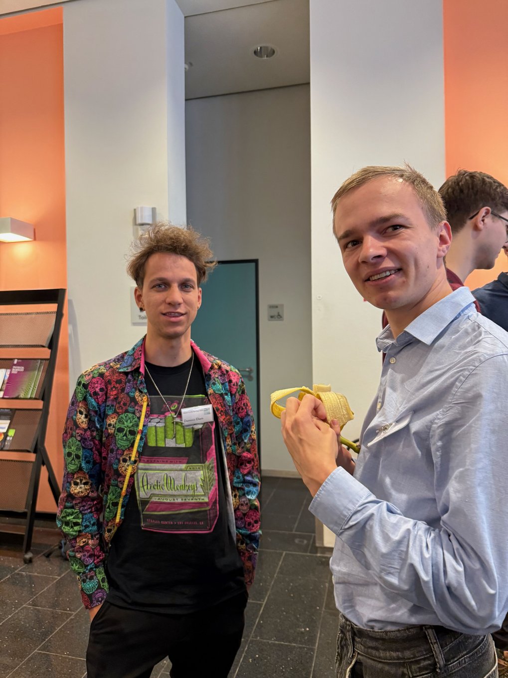 Two individuals engaged in conversation inside a building, with one person casually holding a banana.