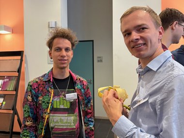 Two individuals engaged in conversation inside a building, with one person casually holding a banana.