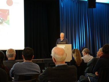 A speaker at a podium marked "Bildungskongress" addresses seated attendees