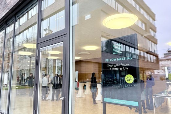 Durch die Glasfenster sieht man die Leute bei einem Wissenschaftstreffen in einem modernen Gebäude.