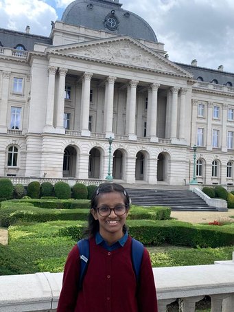 Ananya stands in front of a large building with columns in the background, surrounded by manicured gardens