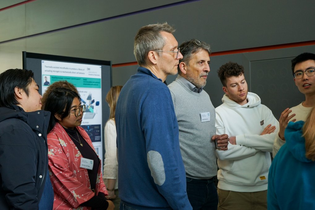 Several individuals are gathered near a presentation poster, discussing its content.