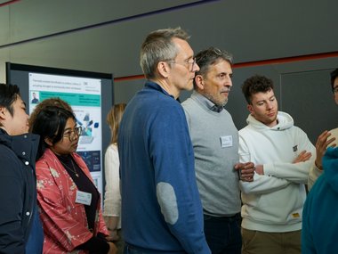 Several individuals are gathered near a presentation poster, discussing its content.