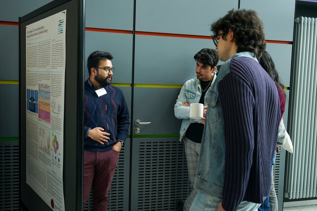 Several individuals are gathered near a presentation poster, discussing its content.