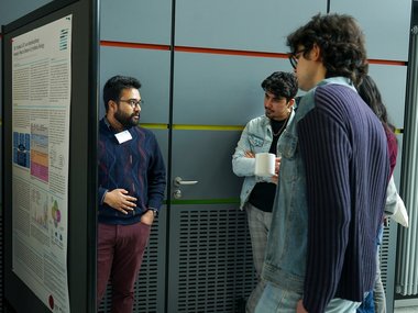 Several individuals are gathered near a presentation poster, discussing its content.