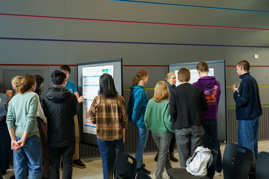 Several individuals are gathered near a presentation poster, discussing its content 