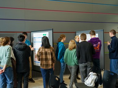 Several individuals are gathered near a presentation poster, discussing its content
