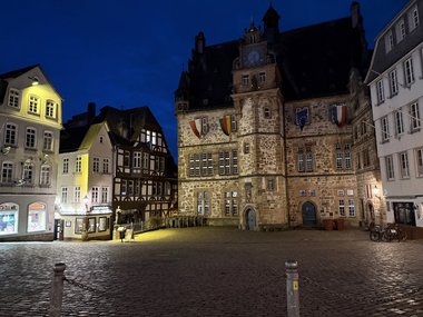 The illuminated historic Marburg City Hall on a cobblestone square with flags at dusk.
