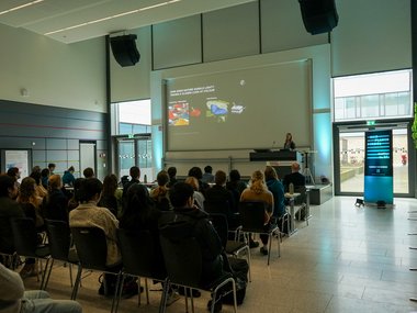 Attendees in a conference room focused on a presentation on a large screen.