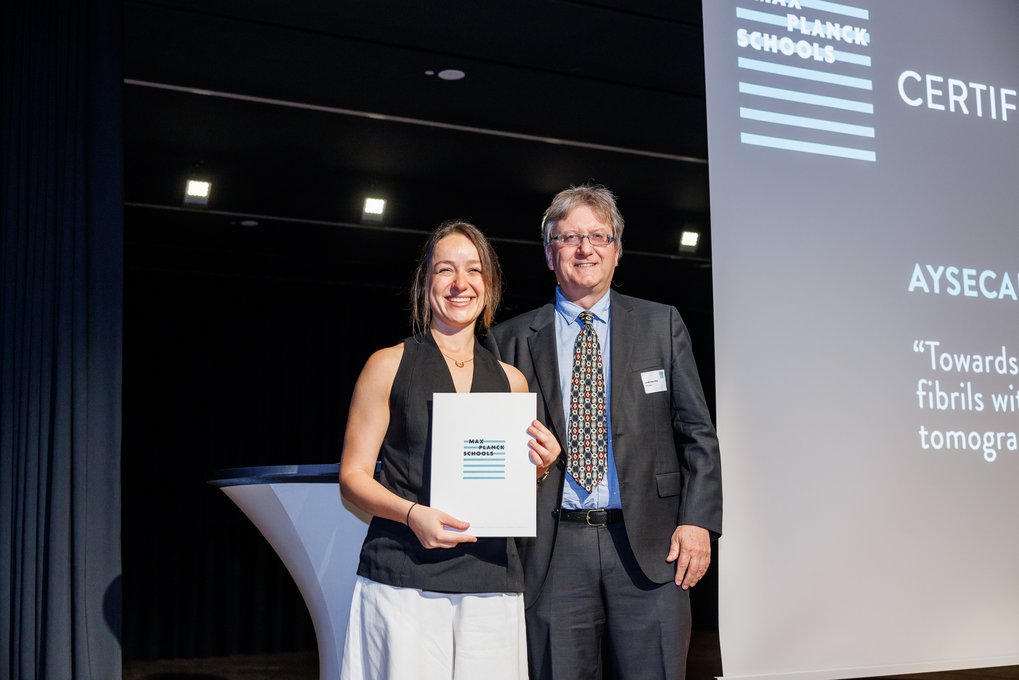 Aysecan Ünal smiling holding a Max Planck Schools certificate, standing beside Jan-Michael Rost in formal attire during an award ceremony.