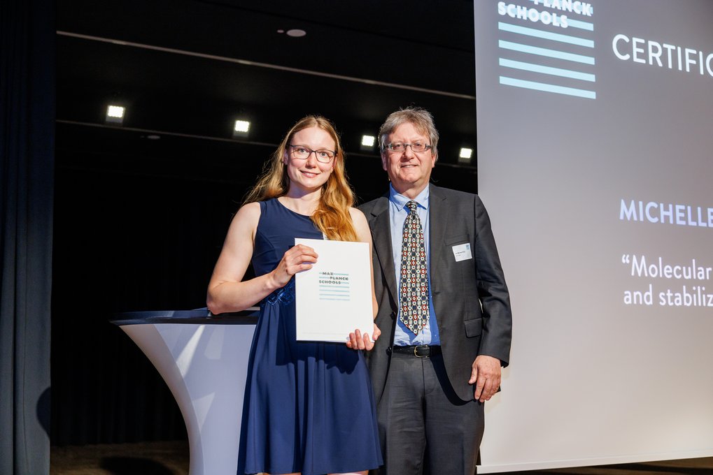 Michelle Kemper holding a certificate standing next to Jan-Michael Rost in a suit.