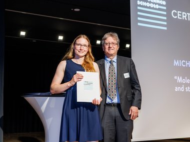 Michelle Kemper holding a certificate standing next to Jan-Michael Rost in a suit.