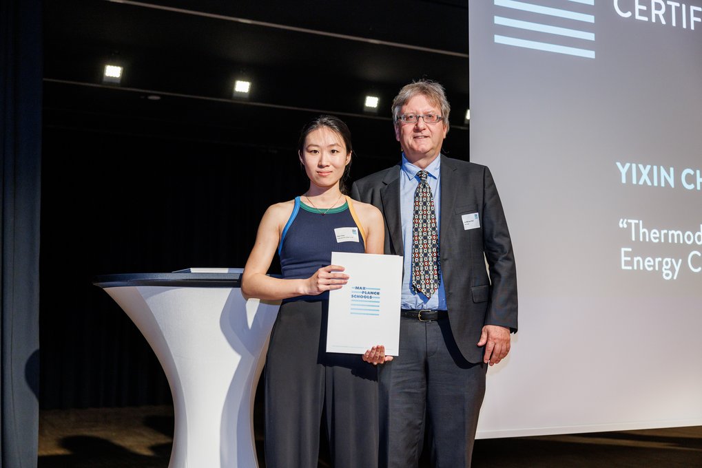Yixin Chen and Jan-Michael Rost posing on stage during the graduation ceremony, with Yixin holding a certificate.