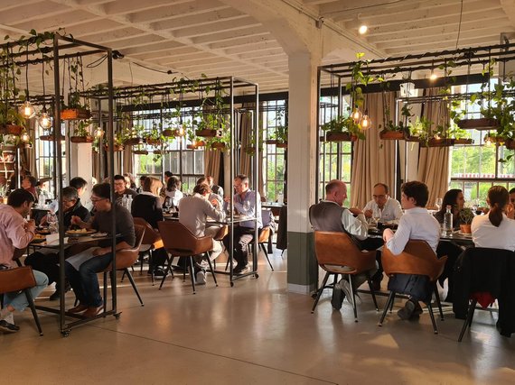 Several diners in a modern, well-lit restaurant with large windows and suspended plant arrangements above the tables.