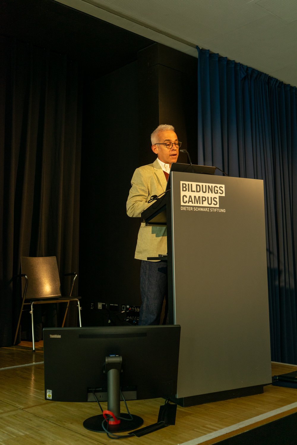Ido Golding standing at a podium with "Bildungs Campus Dieter Schwarz Stiftung" on it, speaking into a microphone.