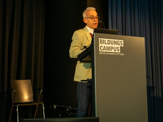 Ido Golding standing at a podium with "Bildungs Campus Dieter Schwarz Stiftung" on it, speaking into a microphone.
