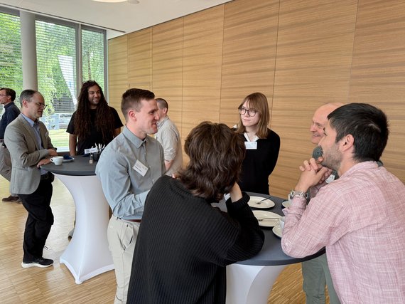 Group of people engaged in conversation around high tables in a modern room.