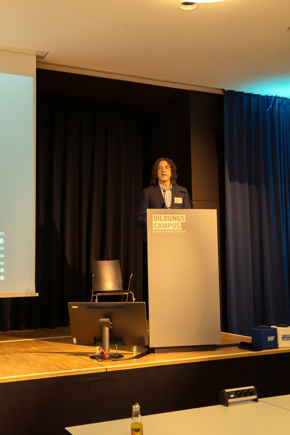 Ernie Glover standing at a podium on a stage with a presentation screen to the side.