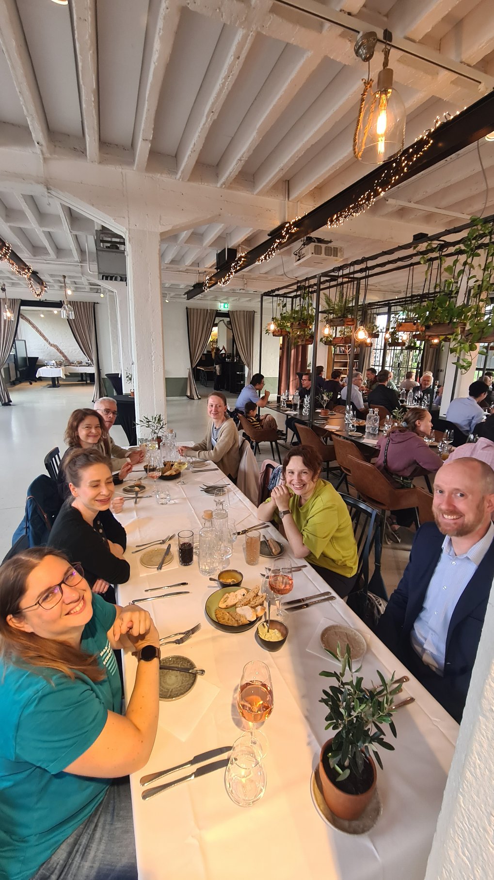 Several individuals gathered at a long table in a modern restaurant setting, enjoying food and beverages.