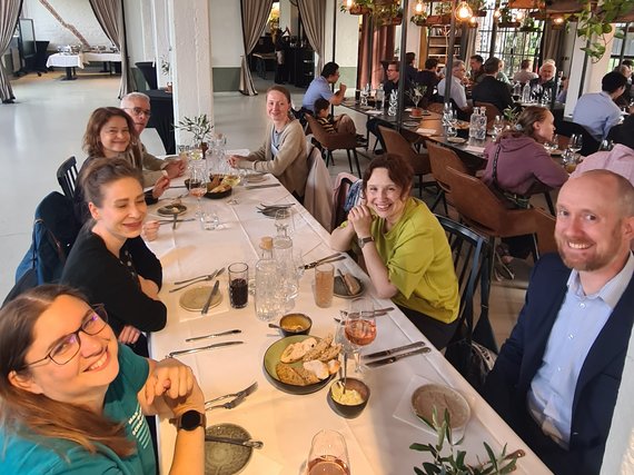 Several individuals gathered at a long table in a modern restaurant setting, enjoying food and beverages.