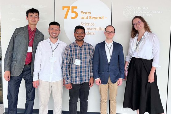 A group of five MtL Ph.D. candidates posing in front of a wall displaying the words “75 Years and Beyond – Science Transcending Borders” and the logos of the Lindau Nobel Laureate Meetings.