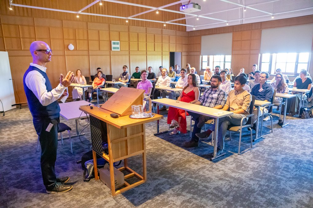 Joachim Spatz delivers a presentation to a group of adults seated at desks in a modern lecture room.