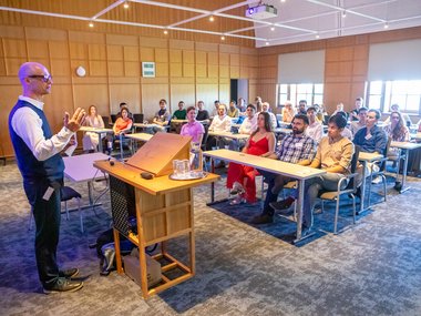 Joachim Spatz delivers a presentation to a group of adults seated at desks in a modern lecture room.