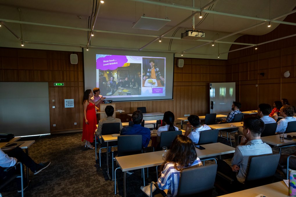 Two presenters speak to an audience in a conference room with a slide about food on the screen.